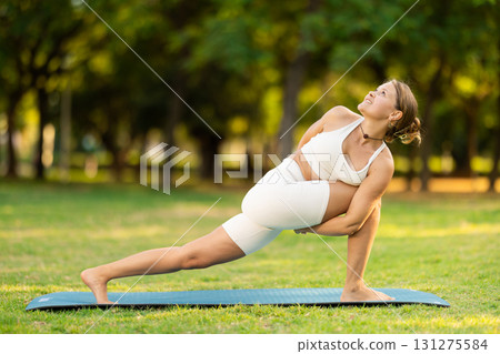 Young woman performing Baddha Parsvakonasana on green meadow 131275584