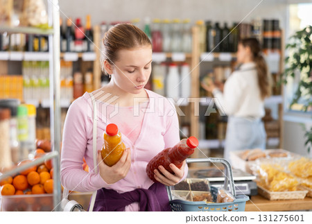 Young girl buyer chooses tomato and peach juices Young girl buyer chooses tomato and peach juices 131275601