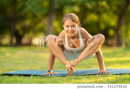 Girl performing shoulder-pressing pose Bhujapidasana in summer park 131275610
