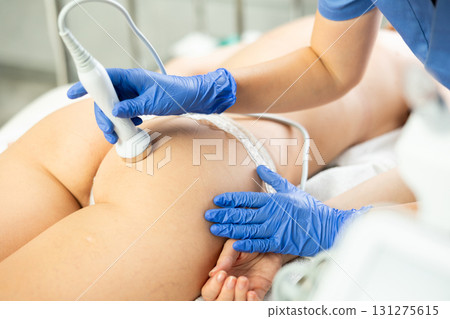 Professional cosmetician performing hardware body treatment, electric massage and moisturizing bottom layer of skin for young woman in clinic of esthetic cosmetology Professional cosmetician performing hardware body treatment, electric massage and moisturizing bottom layer of skin for young woman in clinic of esthetic cosmetology 131275615