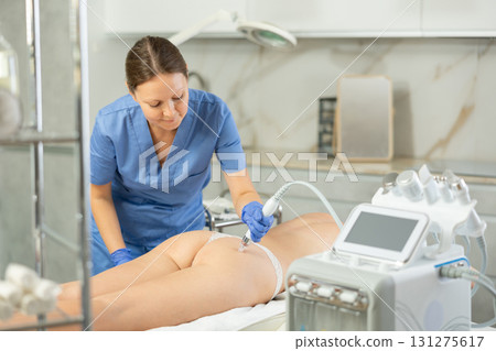 Cosmetologist in rubber gloves does rf-lifting procedure on woman body and buttocks use cosmetology device with hydrogen and oxygen small bubbles, absorb blackheads and deeply clear skin. Professional Cosmetologist in rubber gloves does rf-lifting procedure on woman body and buttocks use cosmetology device with hydrogen and oxygen small bubbles, absorb blackheads and deeply clear skin. Professional 131275617