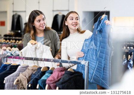 Joyful young women choosing between white and blue waistcoats in a clothing store Joyful young women choosing between white and blue waistcoats in a clothing store 131275618