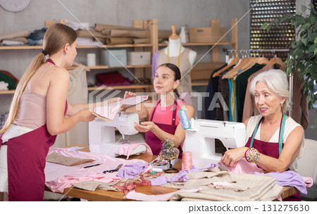 Two seamstresses work with sewing machines, and interact with girl assistant. 131275630