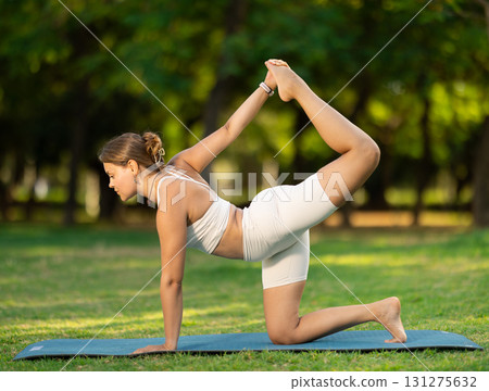 Young girl performing tiger pose during yoga session in summer park 131275632