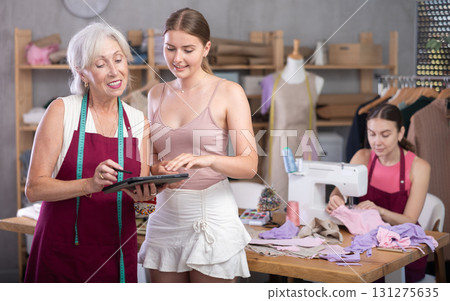 Mature female seamstress showing a sketch of clothes to a client Mature female seamstress showing a sketch of clothes to a client 131275635