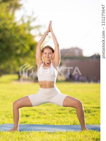 Girl in park on green grass of lawn performs utkata konasana Girl in park on green grass of lawn performs utkata konasana 131275647