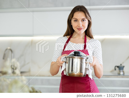 Portrait of positive housewife in an apron with pot of soup in her hands Portrait of positive housewife in an apron with pot of soup in her hands 131275680