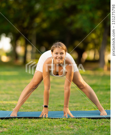Cheerful girl practicing Prasarita Padottanasana on green summer glade 131275798