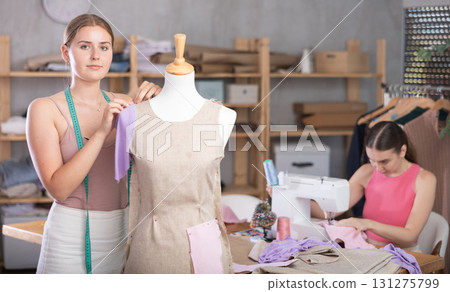 young dressmaker stands near a mannequin with a seamstress in the background 131275799