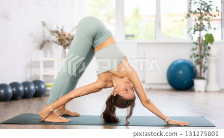 Young woman yoga trainer performing forward bend pose on black rug Young woman yoga trainer performing forward bend pose on black rug 131275801