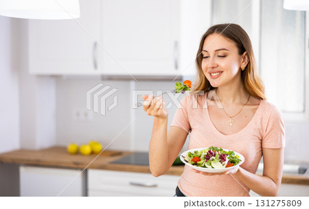 Housewoman eating vegetable salad from plate at home kitchen Housewoman eating vegetable salad from plate at home kitchen 131275809