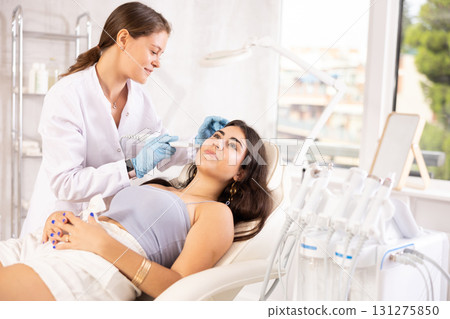European aesthetician making facial beauty procedure with leather knife attachment to brunette girl European aesthetician making facial beauty procedure with leather knife attachment to brunette girl 131275850