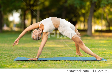 Girl performing Camatkarasana yoga asana in green sunlit park 131275939