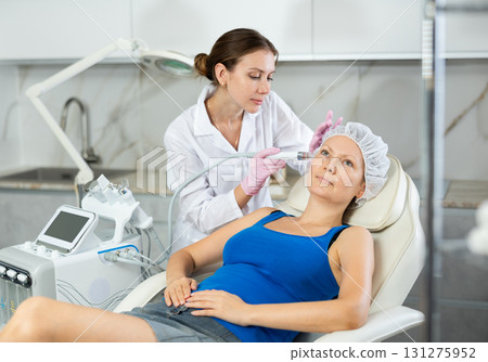 Young female cosmetologist doing cleansing procedure to adult woman 131275952