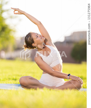 Girl in park on green grass of lawn performs lotus position, padmasana 131275964