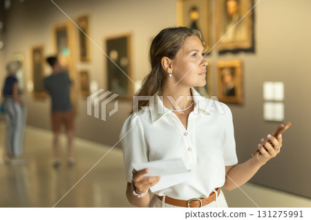 Portrait of young girl visitor with paper guide at the exhibition of paintings in museum Portrait of young girl visitor with paper guide at the exhibition of paintings in museum 131275991