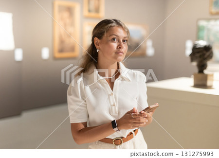 Girl with phone in hands walks around museum hall, view exhibition items Girl with phone in hands walks around museum hall, view exhibition items 131275993