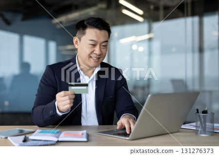 Young Asian man sitting in the office working on a laptop and using a credit card. 131276373