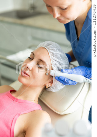 Young girl getting facial rf-lifting procedure of smoothes wrinkles and tightens skin on face in beauty salon. Concept of professional cosmetology 131276419