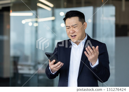 Sad young Asian businessman is in the office, standing looking at the phone and throwing up his hands in frustration. 131276424
