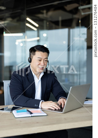Vertical close-up photo of a young Asian businessman in a suit working in the office with a laptop. 131276484