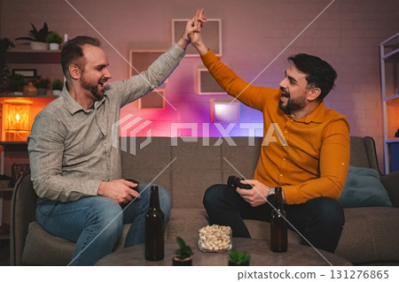 Friends joyfully celebrate gaming victory in a cozy living room during a late night gathering filled with laughter and camaraderie Friends joyfully celebrate gaming victory in a cozy living room during a late night gathering filled with laughter and camaraderie 131276865