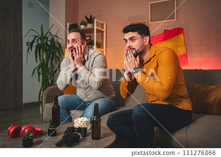 Friends immersed in suspenseful gaming night filled with cheers and snacks in a cozy living room atmosphere Friends immersed in suspenseful gaming night filled with cheers and snacks in a cozy living room atmosphere 131276866