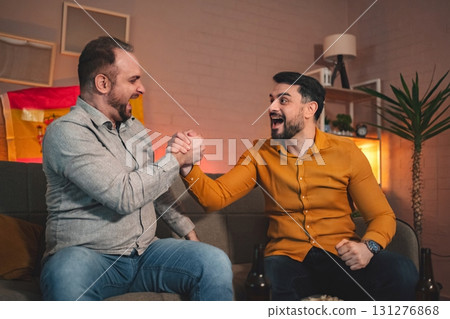 Two friends celebrate in a cozy living room while enjoying a friendly arm wrestling match during a festive gathering Two friends celebrate in a cozy living room while enjoying a friendly arm wrestling match during a festive gathering 131276868