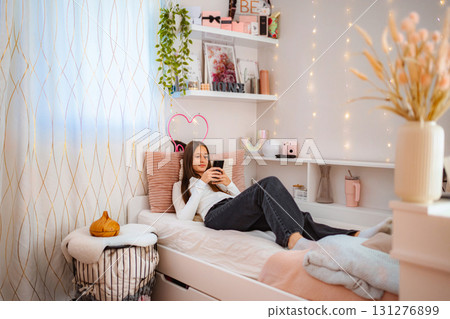 Teenager relaxing in cozy bedroom using smartphone 131276899