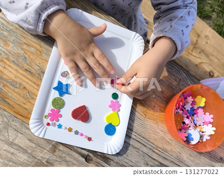 Children's hands create a photo frame, decorating it with glitter and stickers. Children's hands create a photo frame, decorating it with glitter and stickers. 131277022