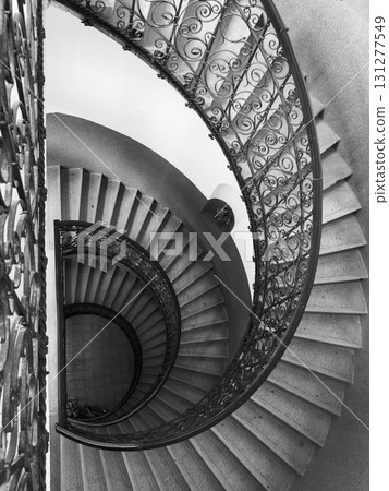 Black and white spiral staircase from above showcasing ornate iron railing and curved steps Black and white spiral staircase from above showcasing ornate iron railing and curved steps 131277549