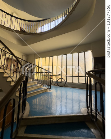 Spiral staircase interior with bicycle by large frosted windows and glossy blue floor 131277556