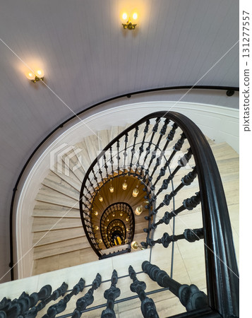 Spiral staircase view from top to bottom with ornate railing and warm wall lights Spiral staircase view from top to bottom with ornate railing and warm wall lights 131277557