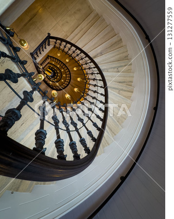 Spiral staircase with ornate wrought iron railing and warm pendant lights viewed from above 131277559
