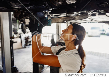 A Skilled Mechanic Deeply Engaged and Working Beneath a Vehicle in the Workshop Environment 131277931