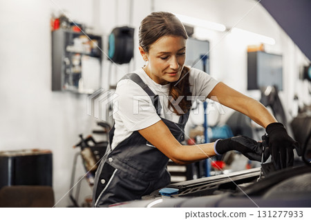 A skilled woman mechanic diligently working on a car engine within an auto repair shop A skilled woman mechanic diligently working on a car engine within an auto repair shop 131277933
