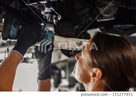 Skilled Mechanic Working Hard Underneath a Vehicle Using Various Power Tools for Repair 131277951