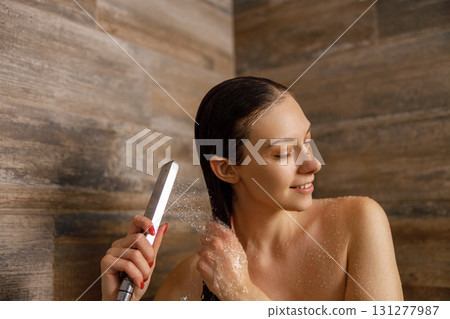 A woman is styling her hair in the shower using a flat iron to achieve a chic look 131277987