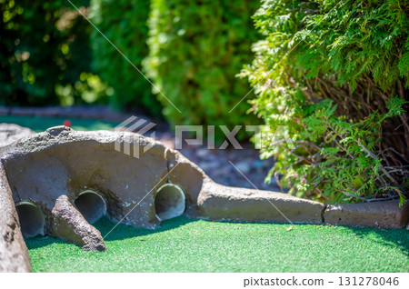 Mini golf course features creative design with tunnels and vibrant green turf during sunny day Mini golf course features creative design with tunnels and vibrant green turf during sunny day 131278046