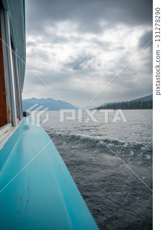 Boat cruising on a calm lake surrounded by mountains under an overcast sky during early morning hours 131278290