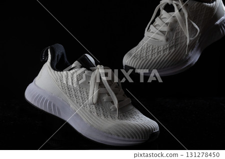 Sneakers with a clean white design are positioned on a solid black surface highlighting their unique texture and style. The laces are tied neatly and the overall appearance is fresh and appealing. 131278450