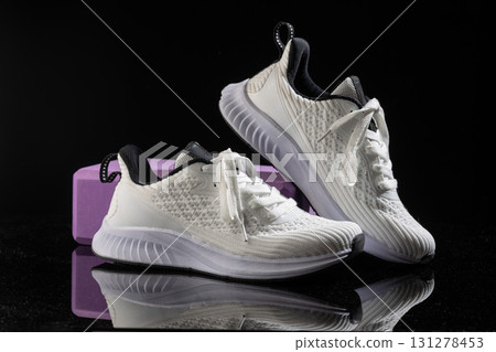 White sneakers rest elegantly on a smooth black surface combined with a vibrant purple block. The design emphasizes comfort and style ideal for various activities. 131278453