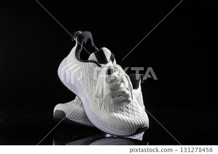 White sneakers are positioned prominently on a smooth black background emphasizing their design and versatility. These shoes suit casual outings and active lifestyles perfectly. 131278456