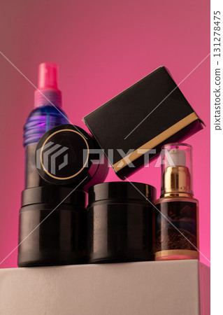 collection of black cosmetic containers and bottles is arranged artistically on a neutral surface. The vibrant pink background creates an eye catching look. 131278475