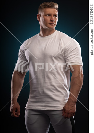 man with an athletic build stands poised in a white T shirt and gray pants. The studio lighting highlights his features creating a powerful look. His expression shows determination and focus. man with an athletic build stands poised in a white T shirt and gray pants. The studio lighting highlights his features creating a powerful look. His expression shows determination and focus. 131278498