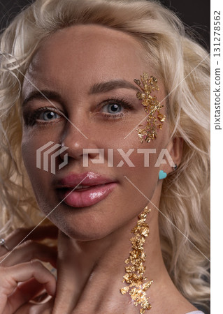 blonde girl smiles confidently showcasing gold glitter adorning her face. She poses gracefully highlighting her unique style and joyful spirit during an artistic moment. blonde girl smiles confidently showcasing gold glitter adorning her face. She poses gracefully highlighting her unique style and joyful spirit during an artistic moment. 131278562