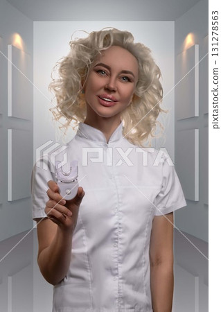 A blonde woman doctor stands proudly in a sleek modern clinic holding a teeth whitening device. Her confident smile and friendly demeanor promote dental health and aesthetics. 131278563