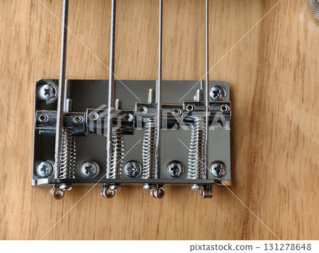 Close-up of bass guitar bridge with metal strings and screws on wooden body 131278648