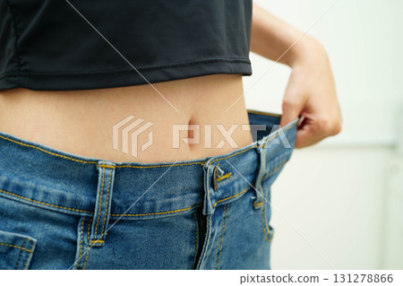 Young Asian woman losing weight wearing loose pants in oversize jeans. 131278866