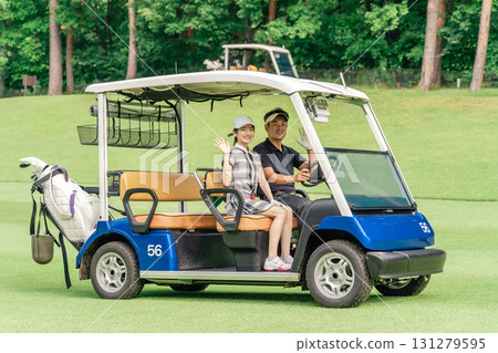 打高爾夫球的男人和女人在高爾夫球場上騎著高爾夫球車 打高爾夫球的男人和女人在高爾夫球場上騎著高爾夫球車 131279595